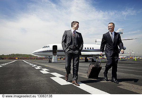 Happy businessmen walking on airport runway against sky