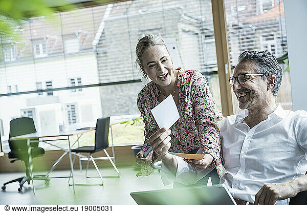 Happy businesswoman and businessman laughing over photograph in office
