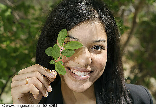 Happy businesswoman covering eye with leaves