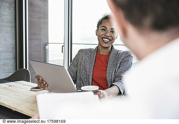 Happy businesswoman discussing by laptop with colleague in office