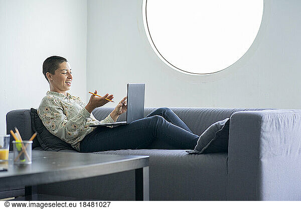 Happy businesswoman doing video call over laptop reclining on sofa at home office