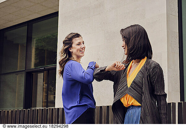 Happy businesswoman elbow bumping with colleague in front of building