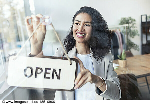 Happy businesswoman hanging open sign on door in studio