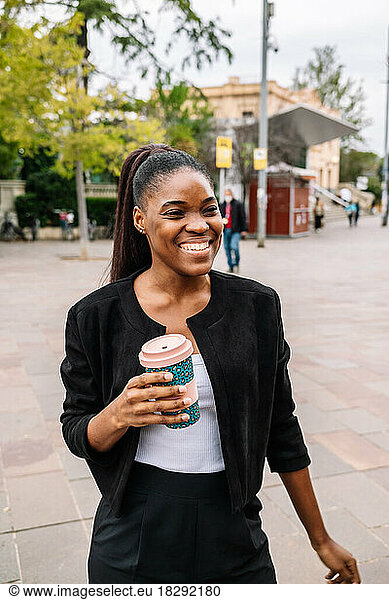 Happy businesswoman holding disposable cup on footpath