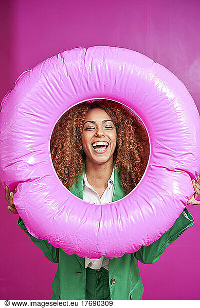 Happy businesswoman looking though inflatable ring against pink background