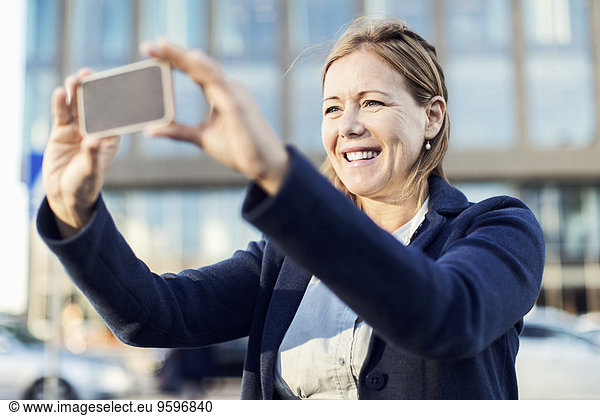 Happy businesswoman photographing with smart phone outdoors