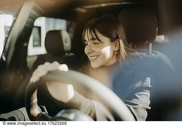 Happy businesswoman sitting inside car seen through mirror