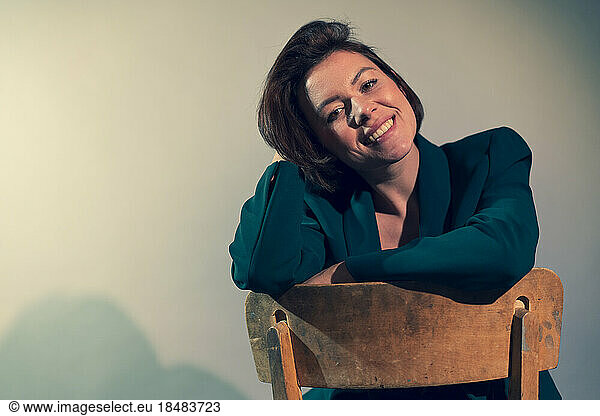 Happy businesswoman sitting on chair against white wall