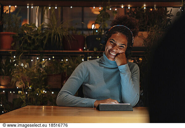 Happy businesswoman sitting with hand on chin at night in office