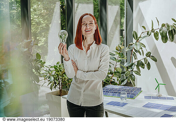 Happy businesswoman standing with light bulb in office