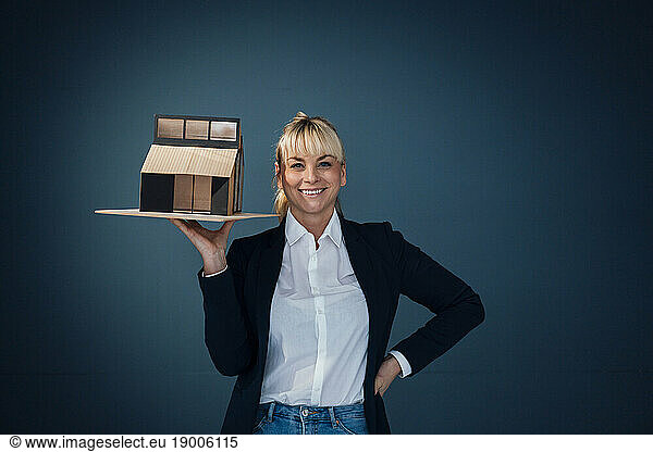 Happy businesswoman standing with model house against blue background
