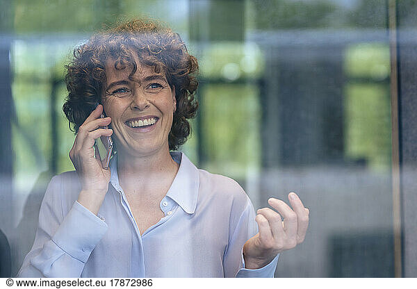 Happy businesswoman talking on mobile phone seen through glass