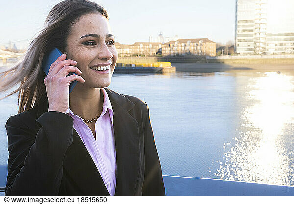 Happy businesswoman talking on smart phone by river