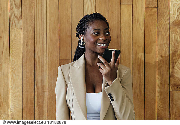 Happy businesswoman talking on smart phone in front of wooden wall