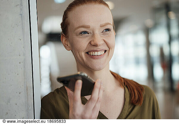 Happy businesswoman talking on speaker phone at office