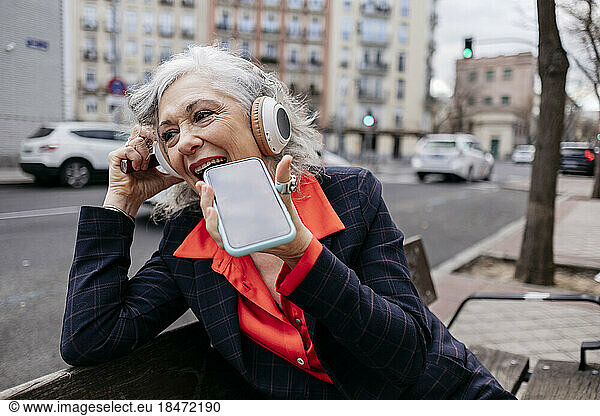 Happy businesswoman talking on speaker phone in city