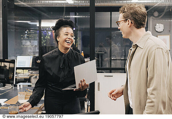 Happy businesswoman talking with businessman while standing at office
