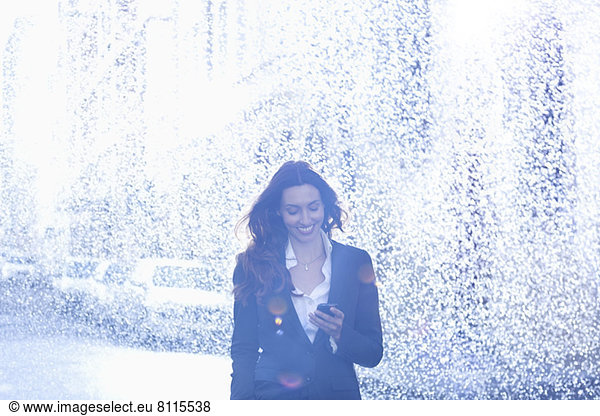 Happy businesswoman text messaging with cell phone in rain