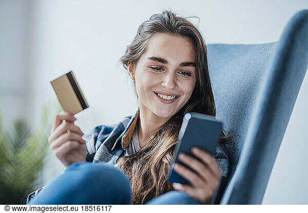 Happy businesswoman using mobile phone and sitting with credit card