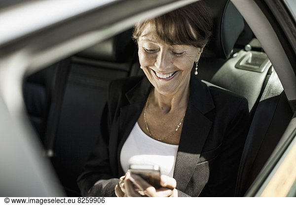 Happy businesswoman using mobile phone in taxi