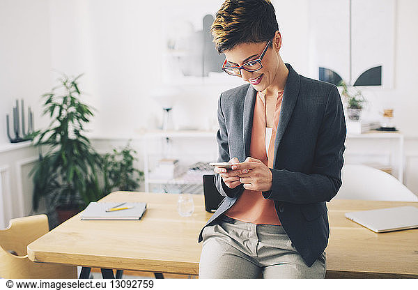 Happy businesswoman using mobile phone while standing at table in office