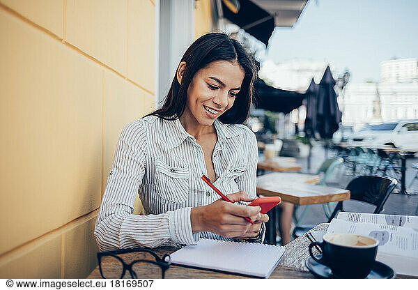 Happy businesswoman using smart phone at sidewalk cafe