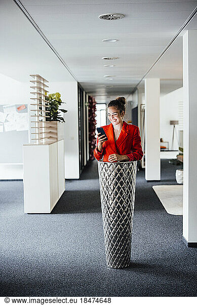 Happy businesswoman using smart phone standing inside planter