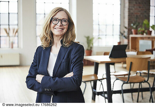 Happy businesswoman wearing eyeglasses standing with arms crossed at home