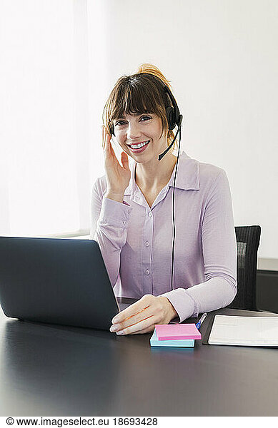 Happy businesswoman wearing headset sitting with laptop at desk
