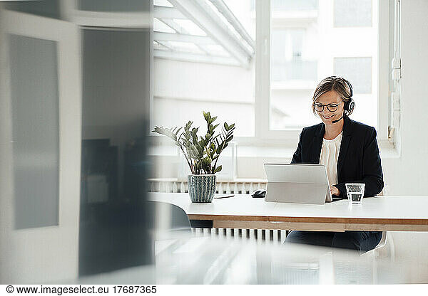 Happy businesswoman wearing headset talking on video call through tablet PC