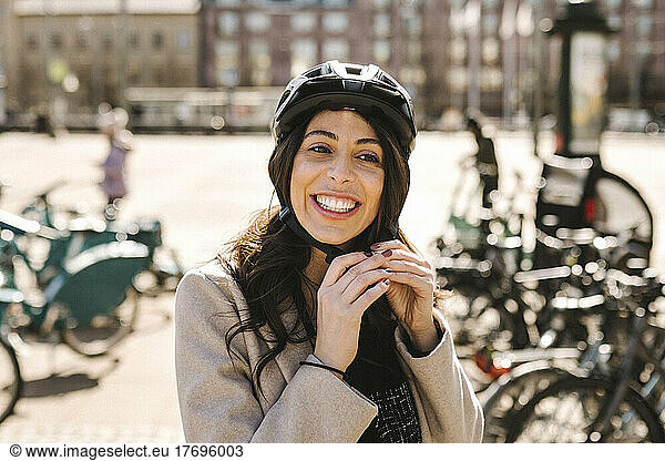 Happy businesswoman wearing helmet at bicycle parking station in city