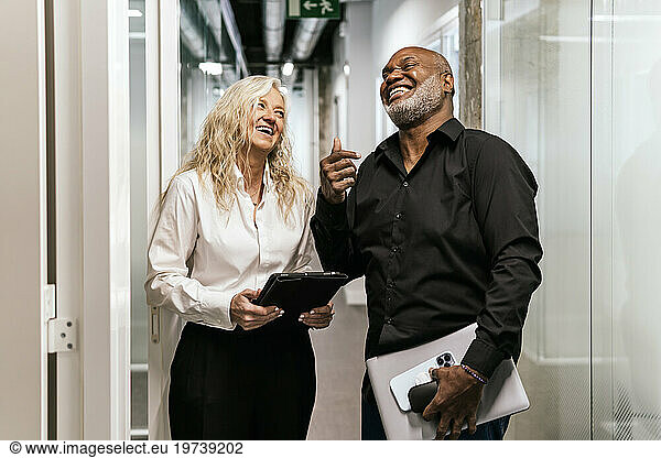 Happy businesswoman with businessman laughing in office corridor