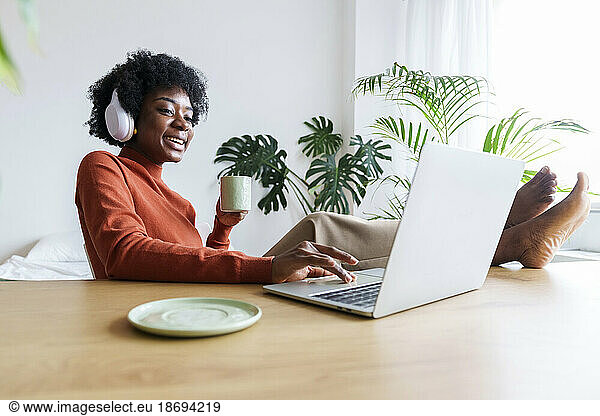 Happy businesswoman with coffee cup working on laptop at desk