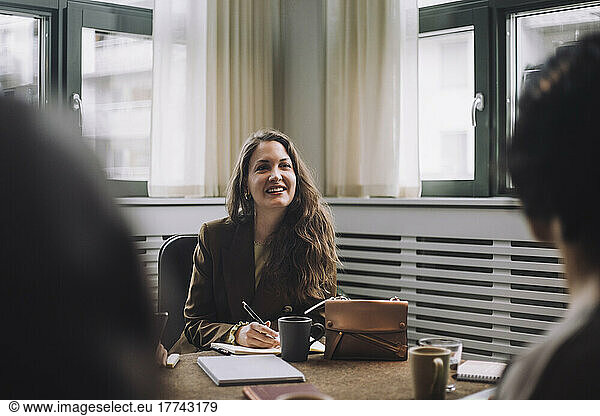 Happy businesswoman with diary sitting at conference table in creative office