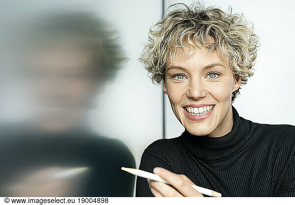 Happy businesswoman with digitized pen leaning on interactive whiteboard