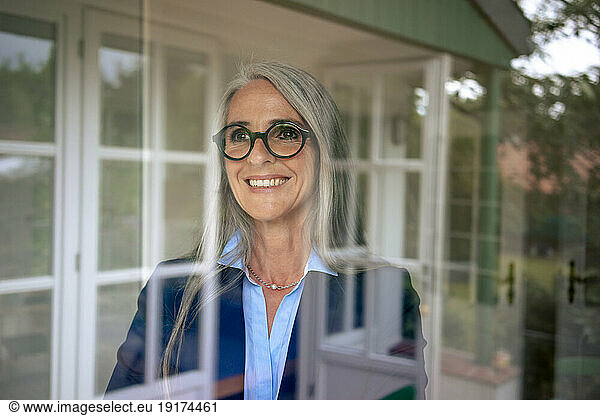 Happy businesswoman with gray hair seen through glass