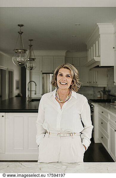 Happy businesswoman with hands in pockets standing in kitchen at home