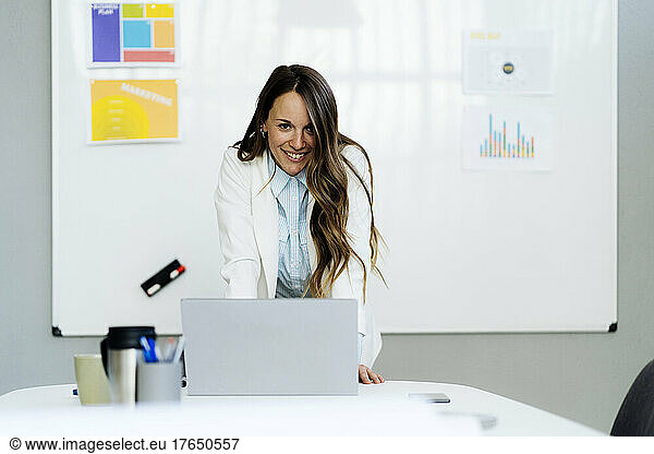 Happy businesswoman with laptop at desk in office