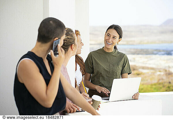 Happy businesswoman with laptop discussing with colleagues