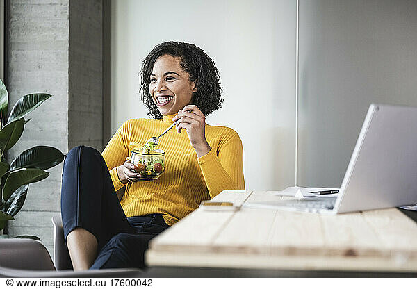 Happy businesswoman with salad bowl at work place