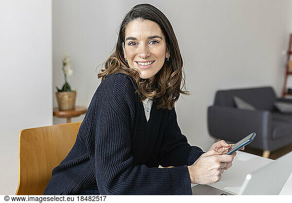 Happy businesswoman with smart phone sitting in office