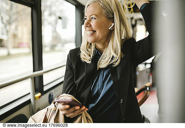 Happy businesswoman with smart phone travelling in bus