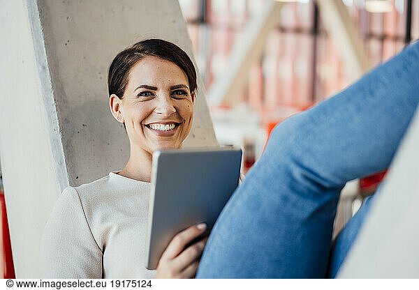 Happy businesswoman with tablet PC on V-shaped column