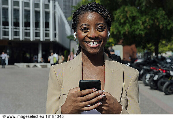 Happy businesswoman with wireless in-ear headphones listening to music in city