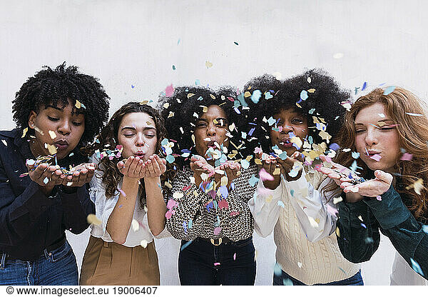 Happy businesswomen blowing confetti in front of wall