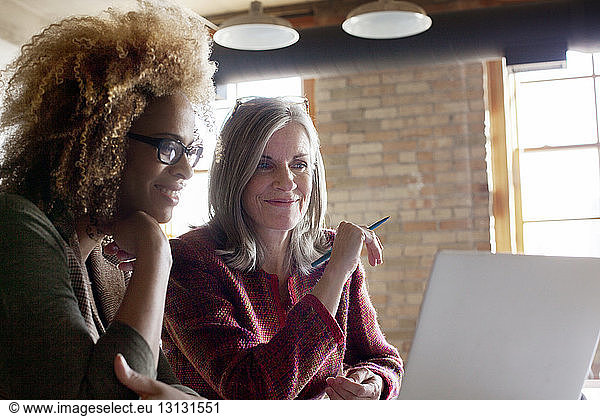 Happy businesswomen using laptop in creative office