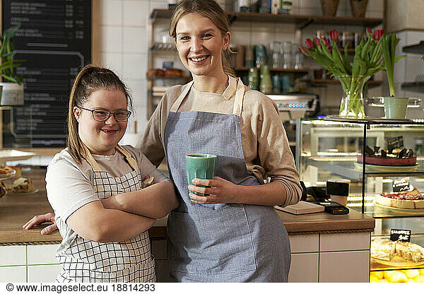 Happy cafe owner with down syndrome standing by colleague in coffee shop