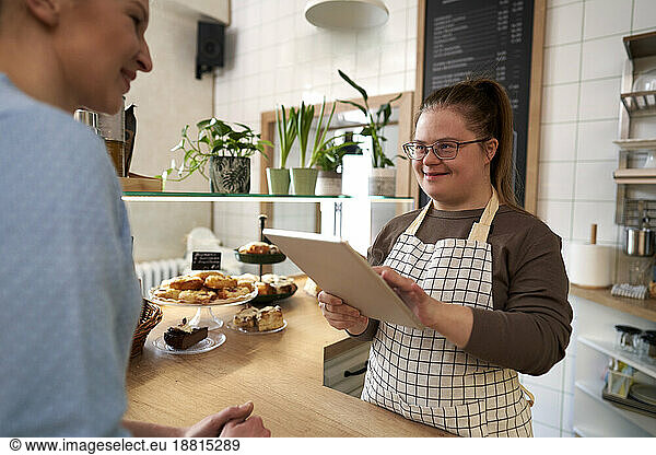 Happy cafe owner with down syndrome taking order of customer through tablet PC