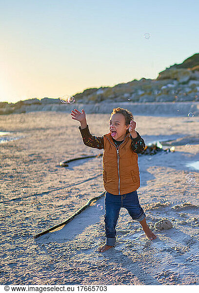 Happy  carefree boy with Down Syndrome playing with bubbles on beach
