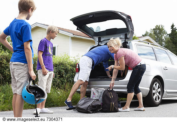 Happy Caucasian family loading luggage in car trunk for picnic